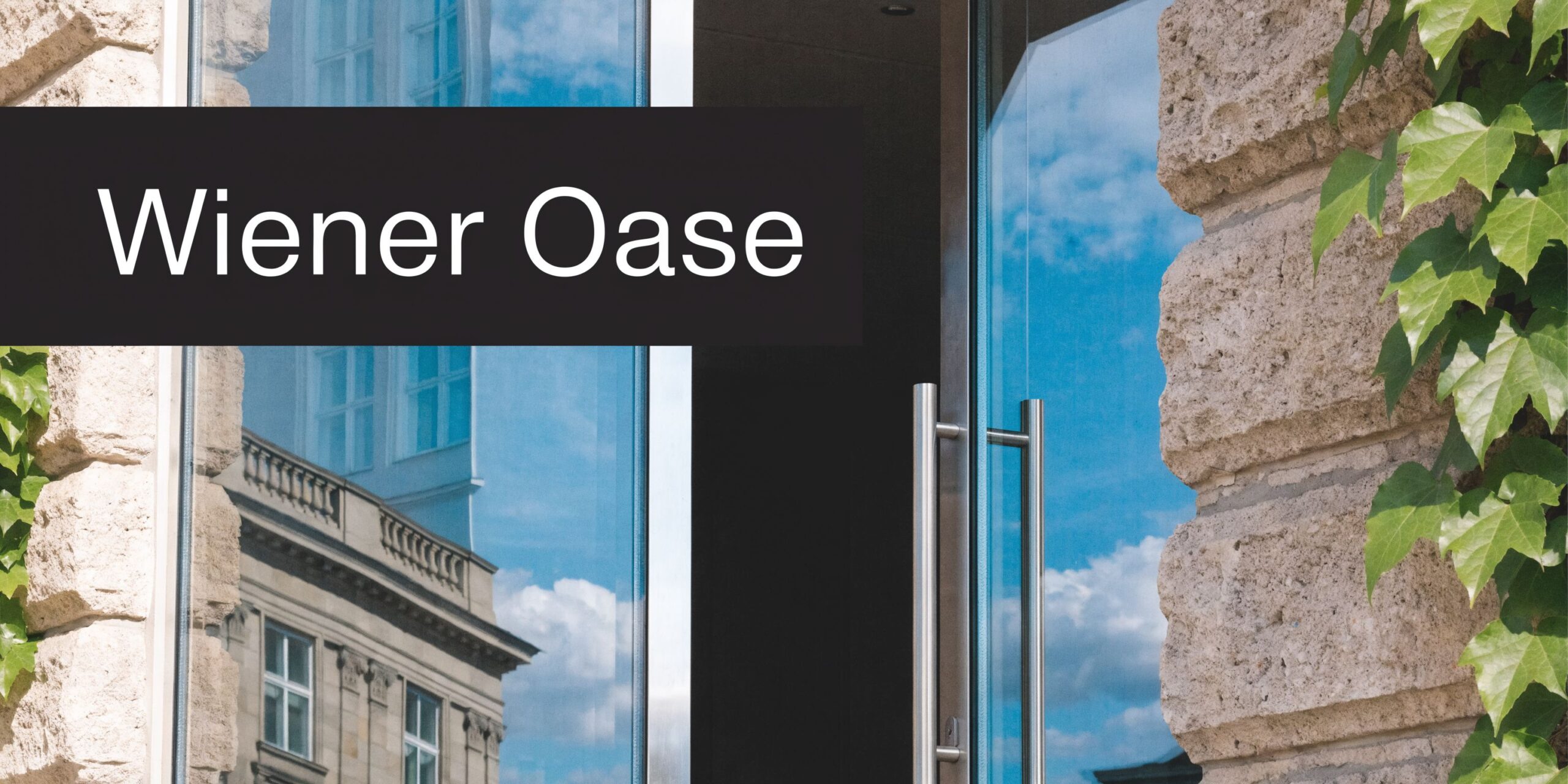 Ein moderner Eingangsbereich mit gläserner Tür, Steinmauer und Pflanzen, beschriftet mit dem Namen Wiener Oase.