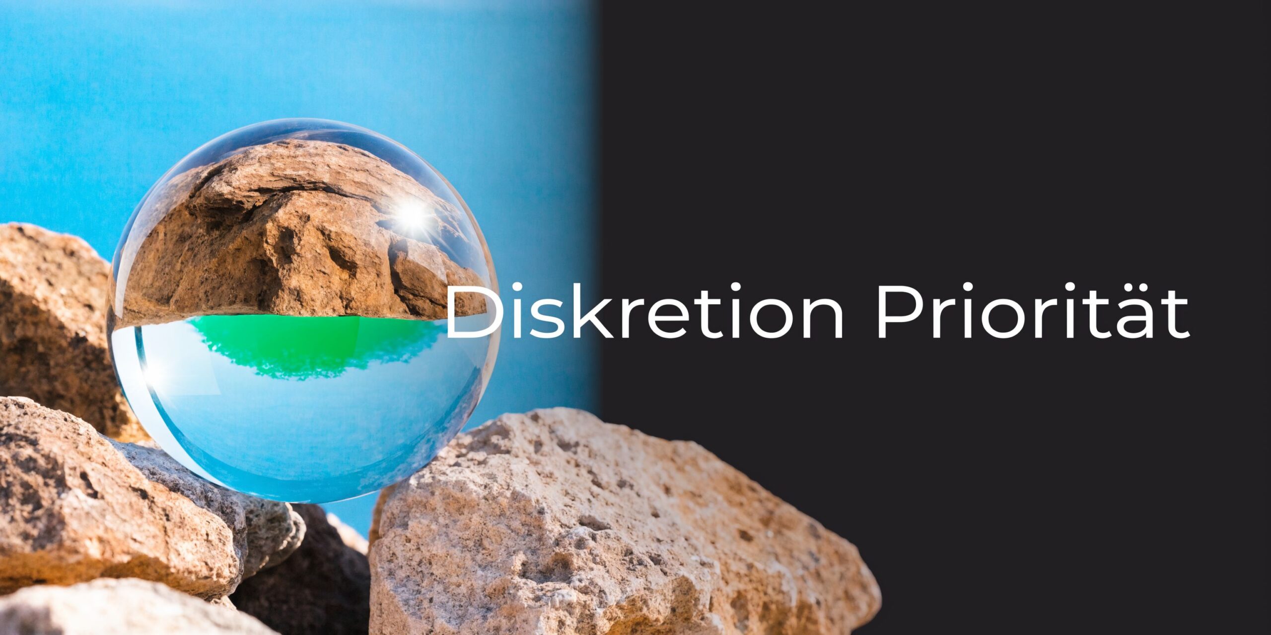 Eine Glaskugel auf Felsen vor einem geteilten Hintergrund mit blauem Himmel und schwarzer Fläche.