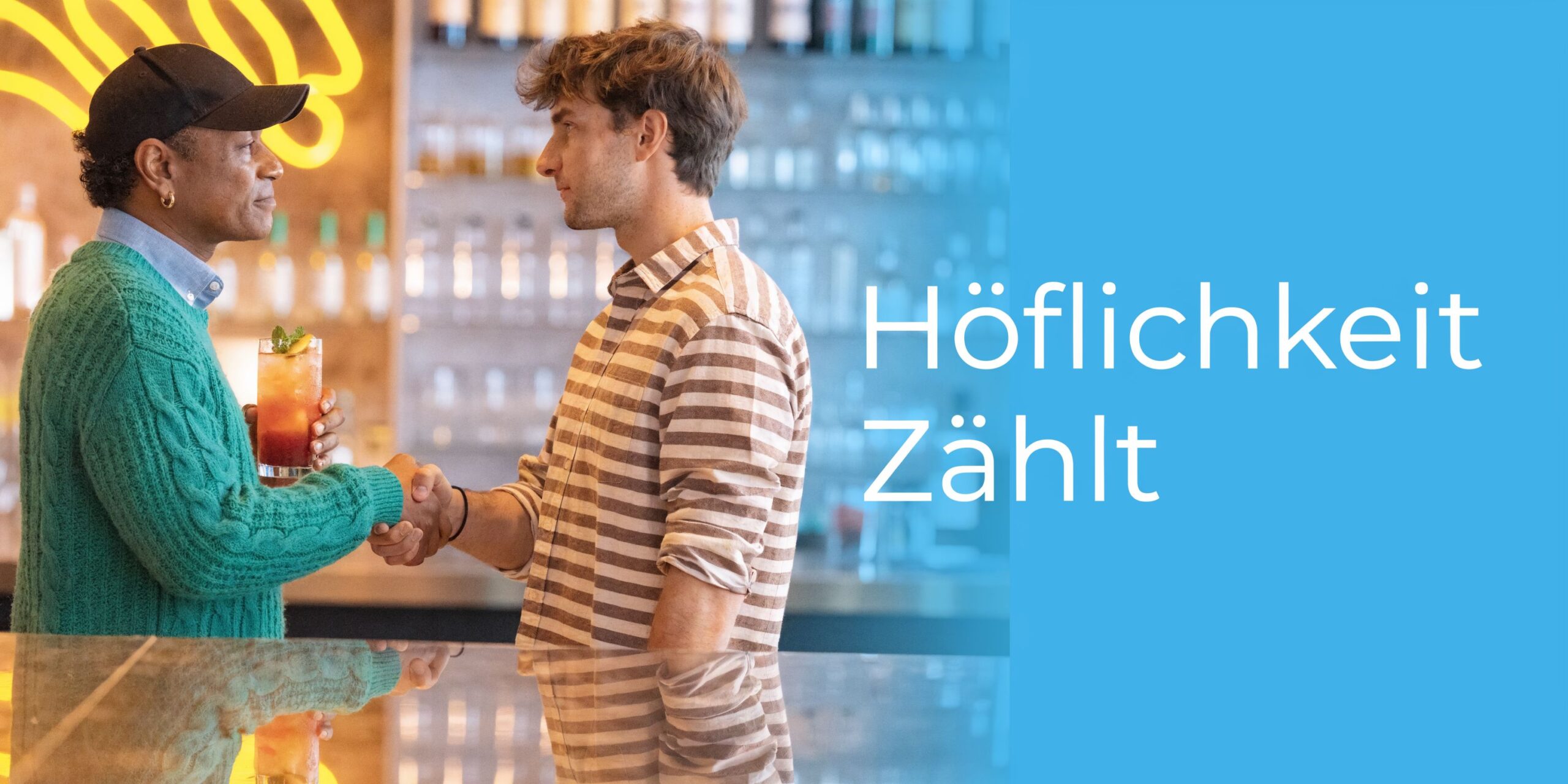 Zwei Männer, einer in einer grünen Strickjacke und ein anderer in einem gestreiften Hemd, schütteln sich die Hände.