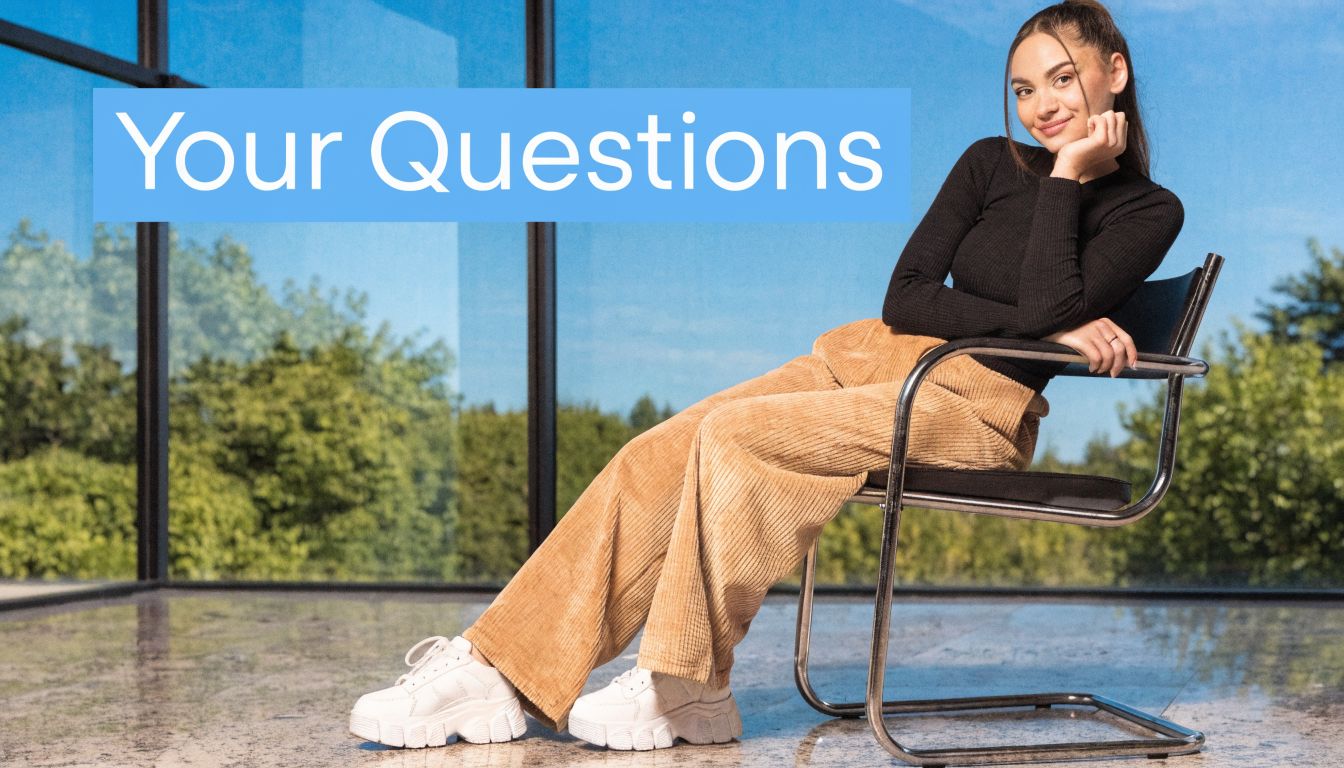 Eine junge Frau in einem schwarzen Pullover und beiger Hose sitzt entspannt auf einem modernen Stuhl.