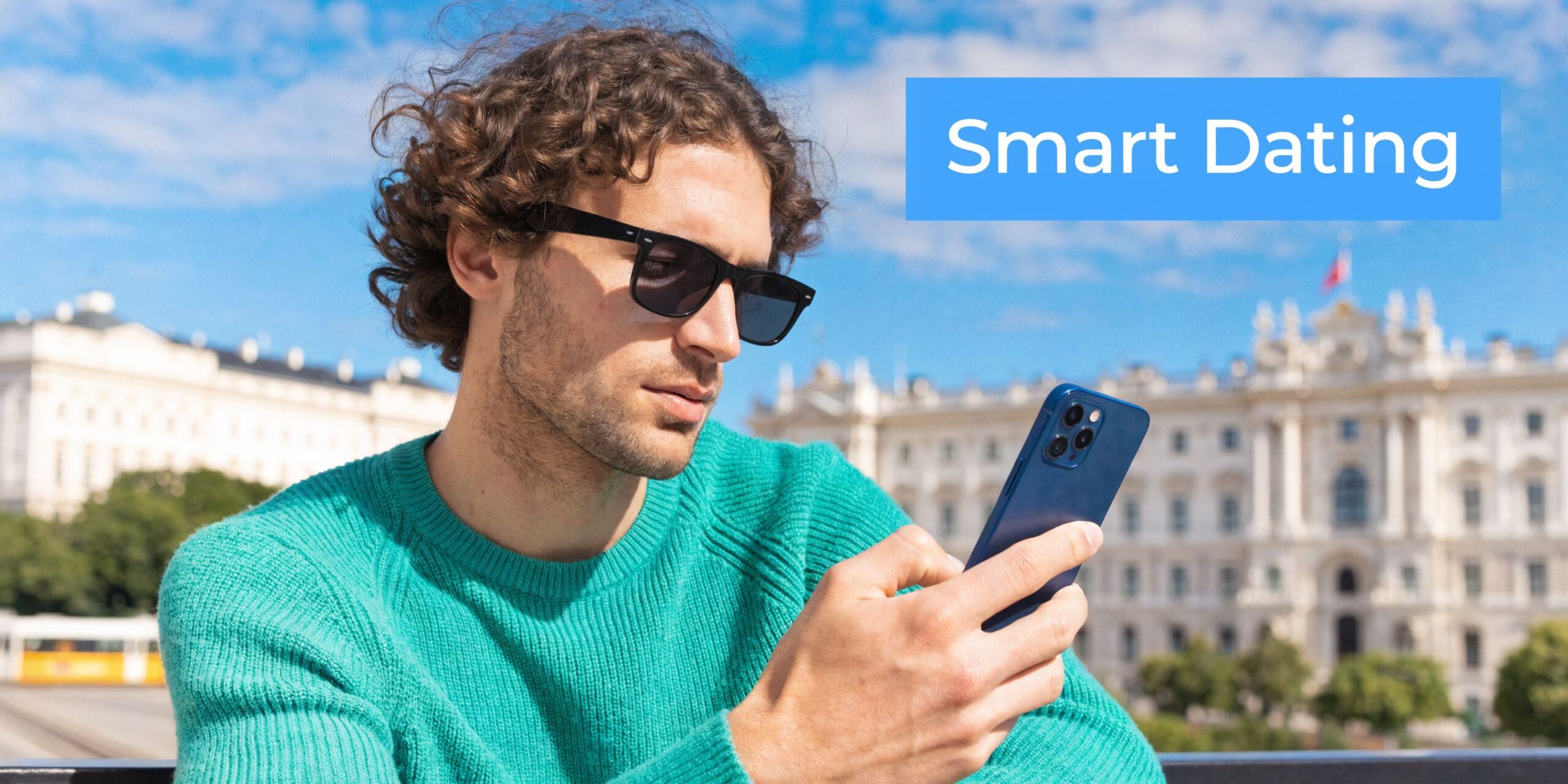 Ein junger Mann mit Sonnenbrille und grünem Pullover schaut vor einer historischen Wiener Kulisse auf sein Smartphone.