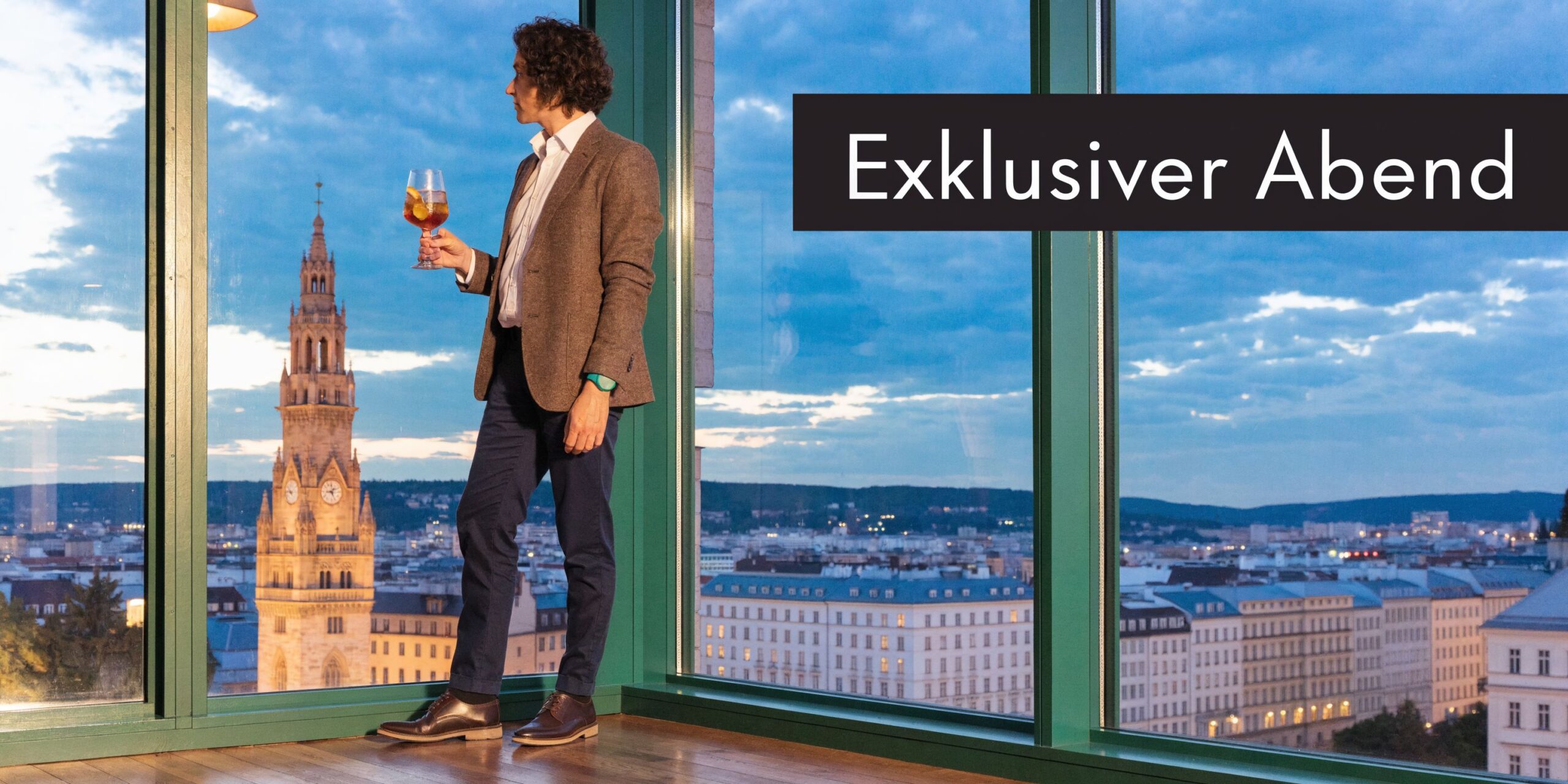 Ein elegant gekleideter Mann mit einem Cocktail steht vor einem Fenster mit Blick über das abendliche Wien.