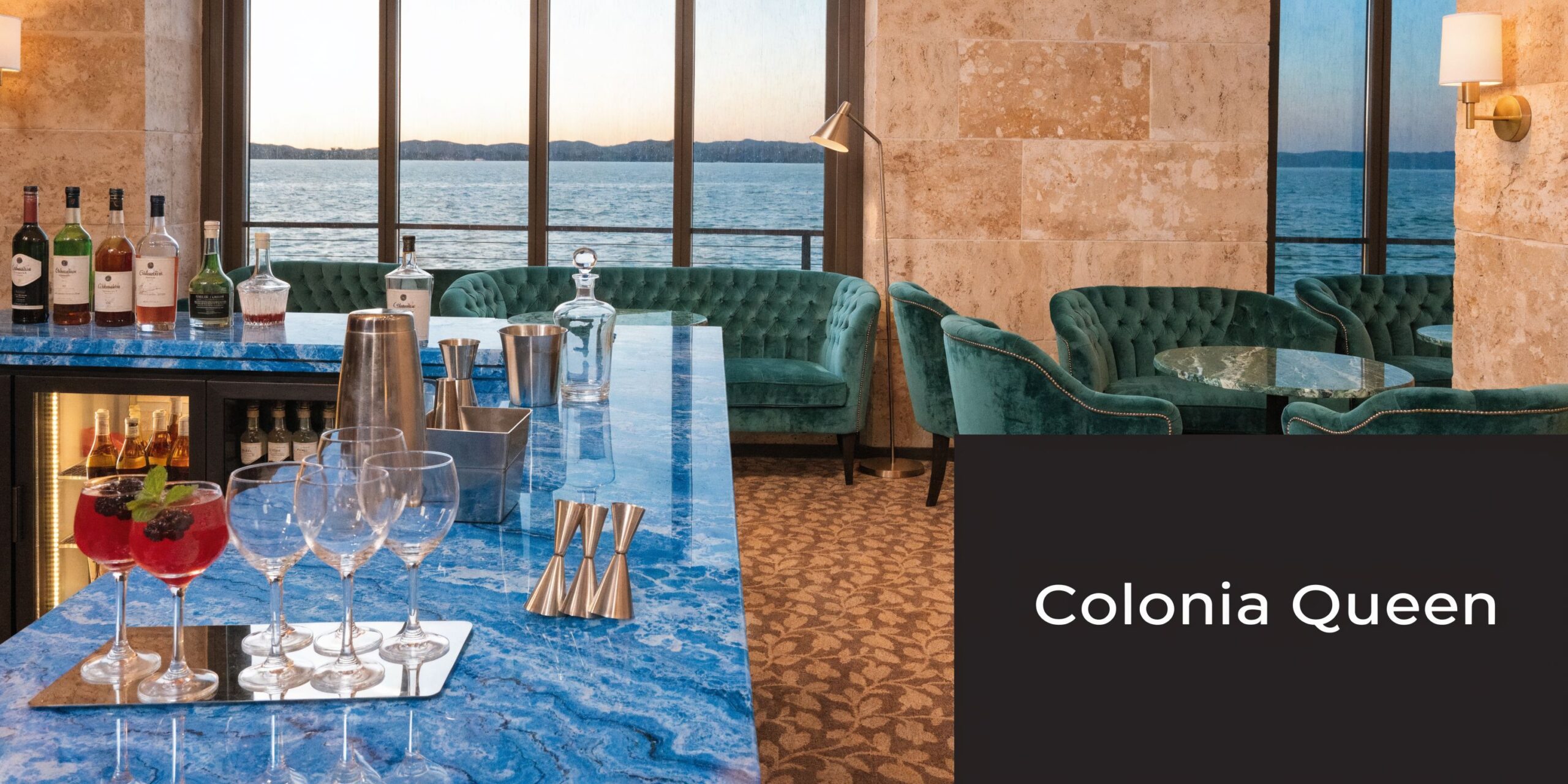 Eine luxuriöse Hotelbar mit türkisfarbener Theke, gemütlichen grünen Sesseln und einem wunderschönen Blick auf das Meer.